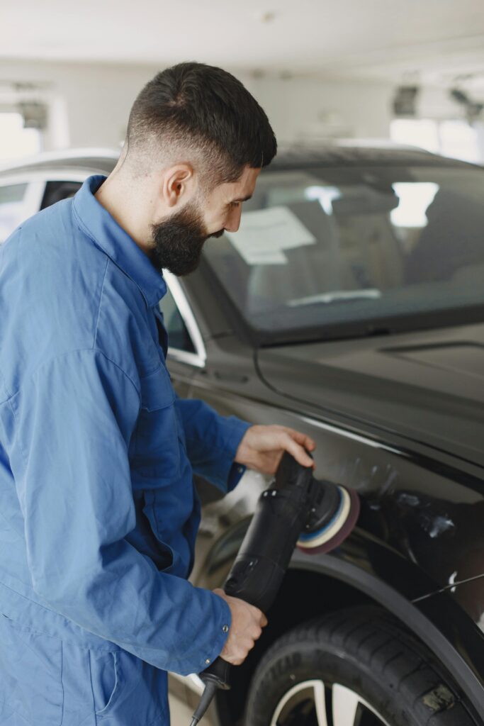 pexels-photo-6870310-6870310 Mechanic wearing blue uniform polishing car body with machine in workshop.